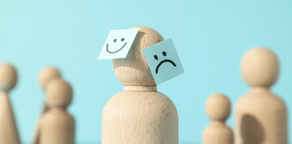 Wooden figure with a smiley face and a sad face sticky notes on its head, representing the contrasting emotional states in bipolar disorder.