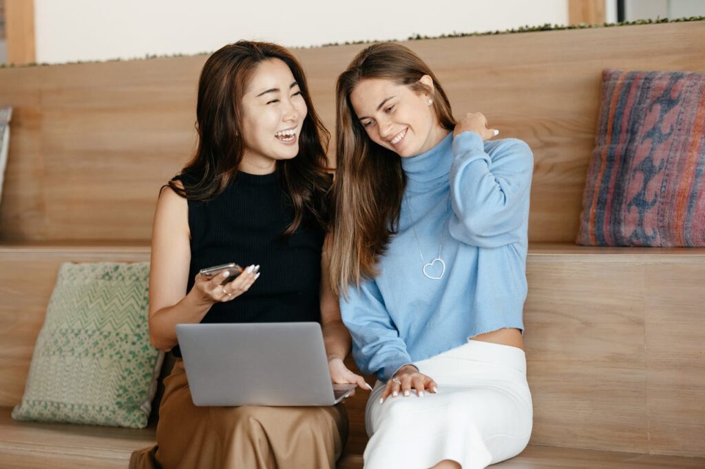 Two females sitting together, one engrossed in her phone and laptop while the other sits aside, illustrating the reduced social connection time associated with high screen time.