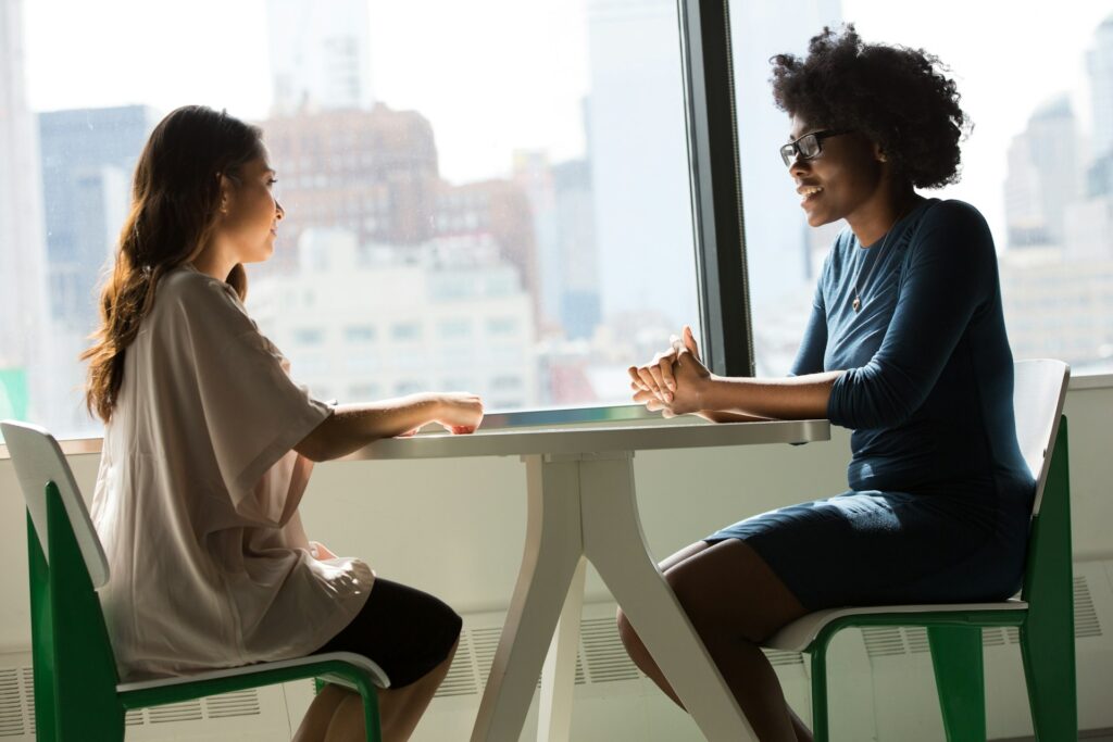 Image of two females seated at a table, one appearing as a patient and the other as a psychologist, engaged in a therapy session.