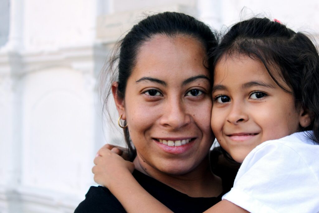 A mom is carrying her little girl on her shoulders.