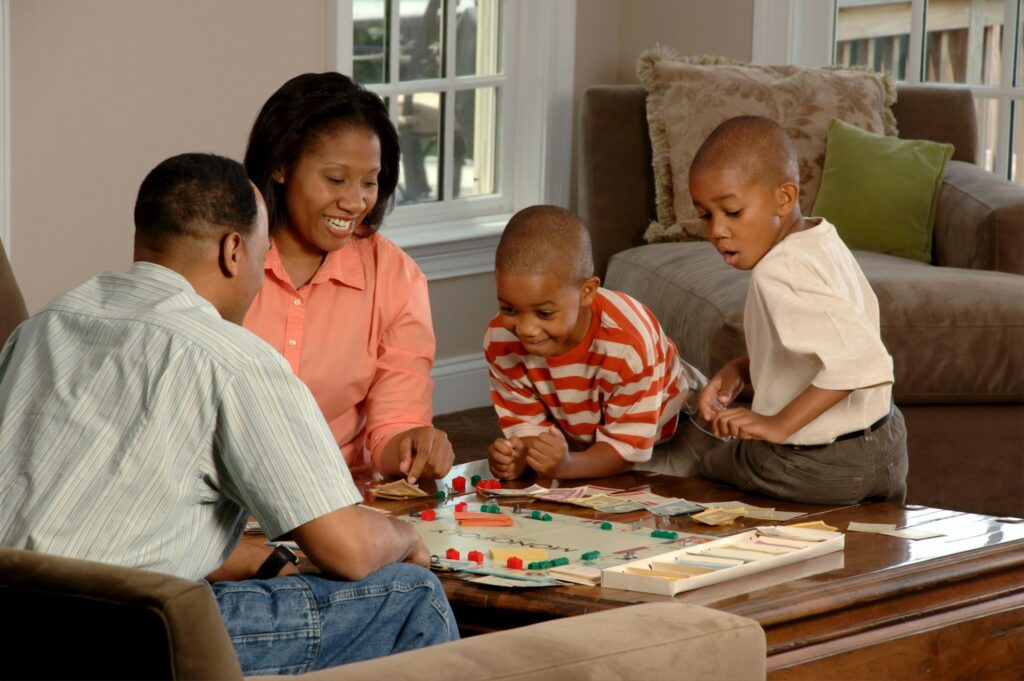 A family is playing a game on a brown table and they look happy.