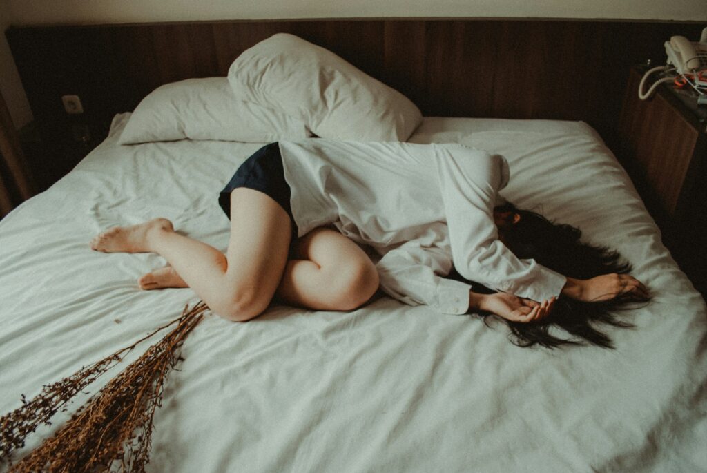 Image of a woman lying uncomfortably on a bed, possibly experiencing severe depression or mental distress. The woman is wearing a white shirt.