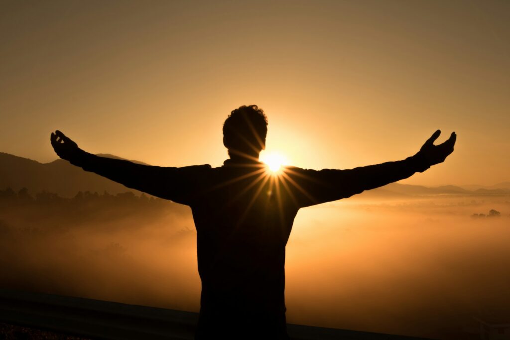 Image of a man with arms wide open, facing the rising sun, symbolizing a welcoming gesture towards life and new beginnings.