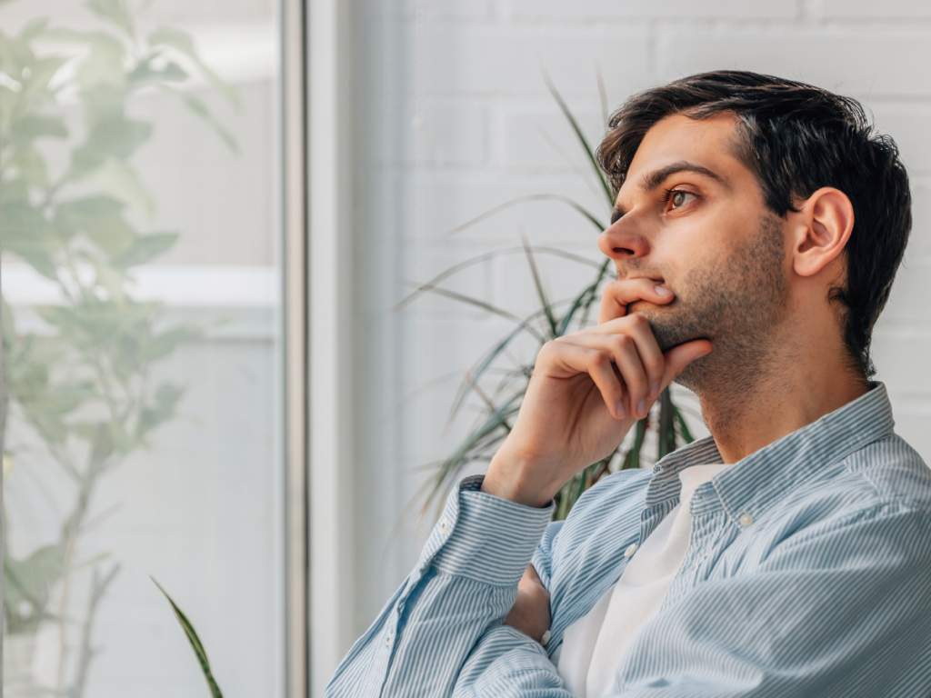 A man sits by a window while thinking. 