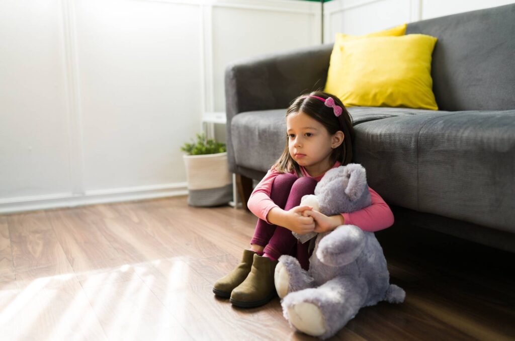 A child sits alone while hugging a toy to show the childhood trauma of neglect.