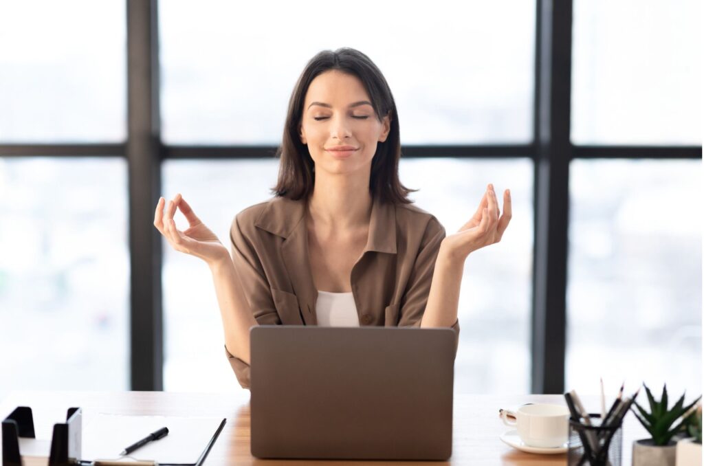 A woman meditates as a stress management technique while at her desk. 