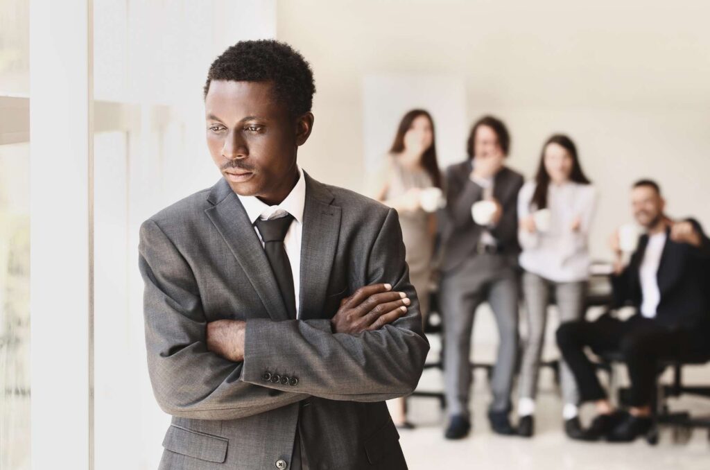 A man in a suit stands apart from other people to show job insecurity.