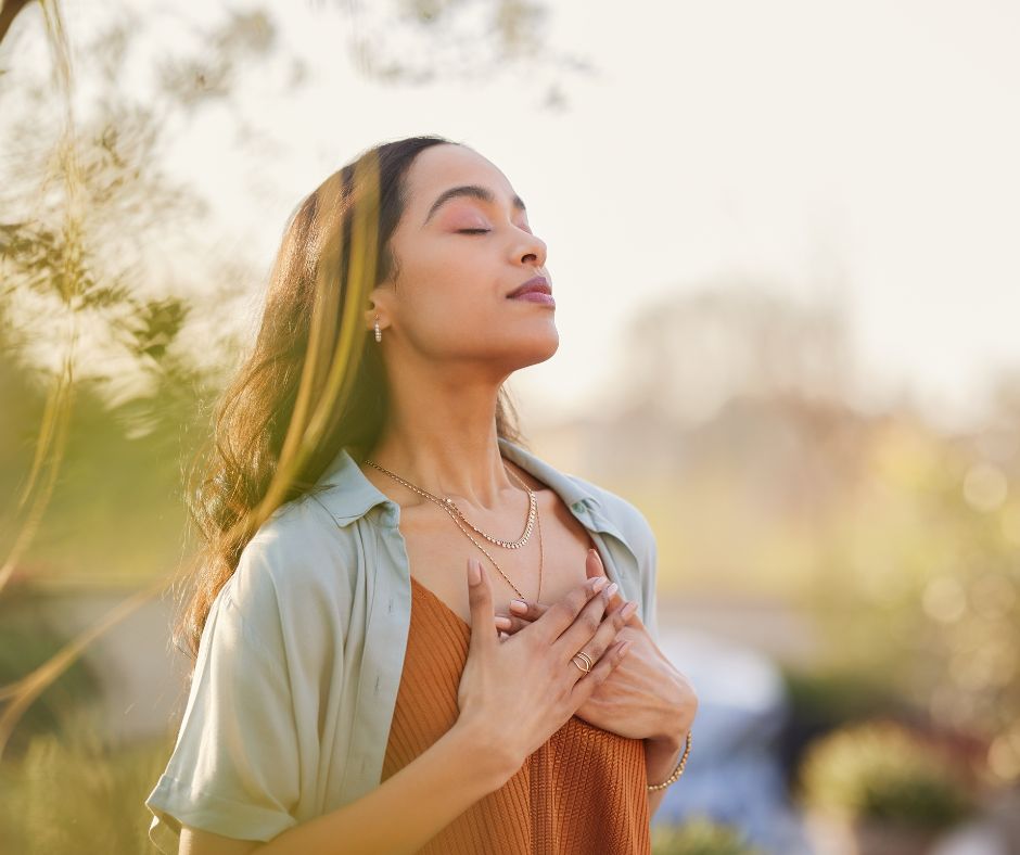 A woman looks relaxed as she practices deep breathing techniques outdoors.