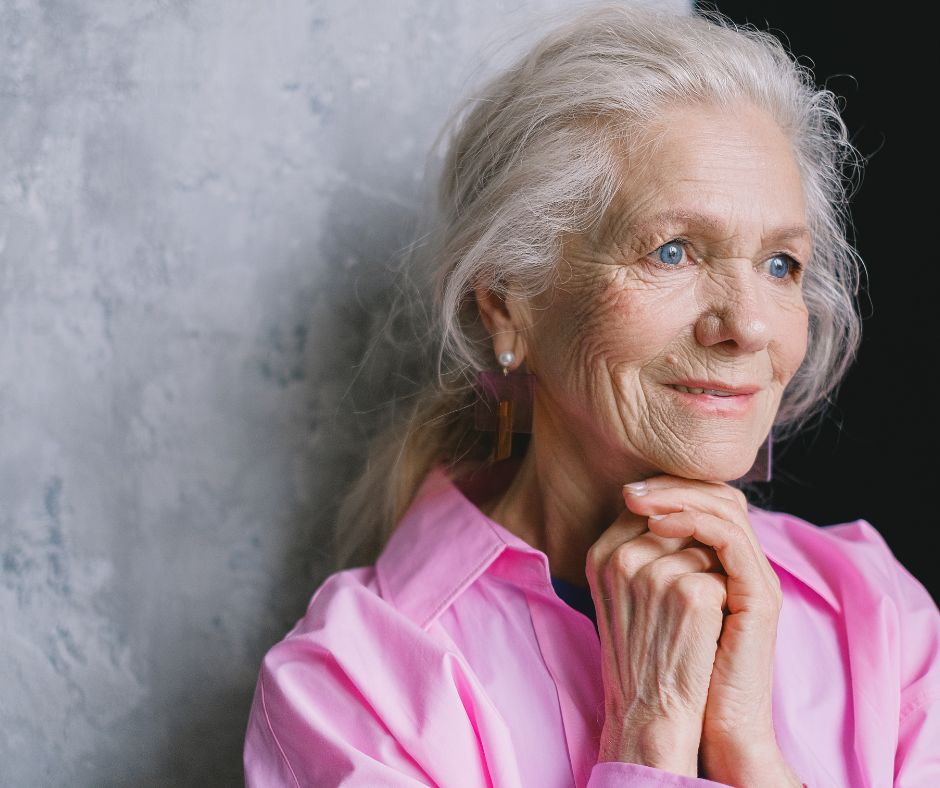 An old woman is smiling with her hands clasped