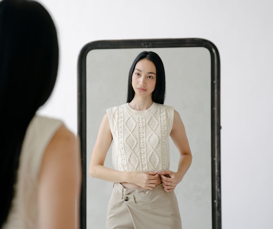 A woman stares at the mirror, unsmiling because of imposter syndrome.