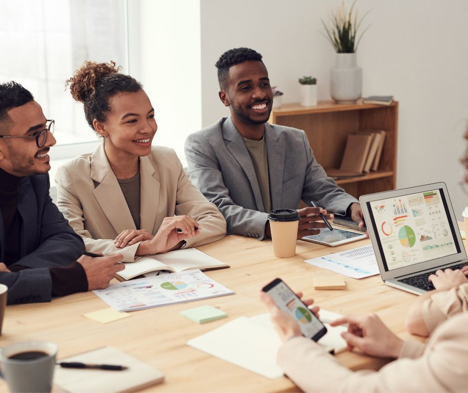 A multi-cultural group of employees, showing no signs of culture shock, sit at a conference table.
